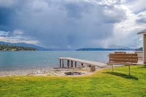 A lakeside view with a wooden dock, a bench, and a building with a balcony. - Lakefront home with kayaks, dock, WiFi, fireplaces, BBQ grill (Hope)