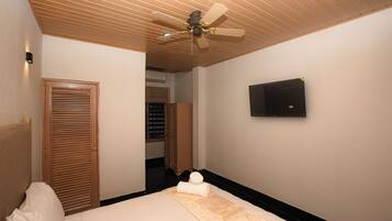 A hotel room with a bed, a ceiling fan, a television, and a wooden wardrobe.