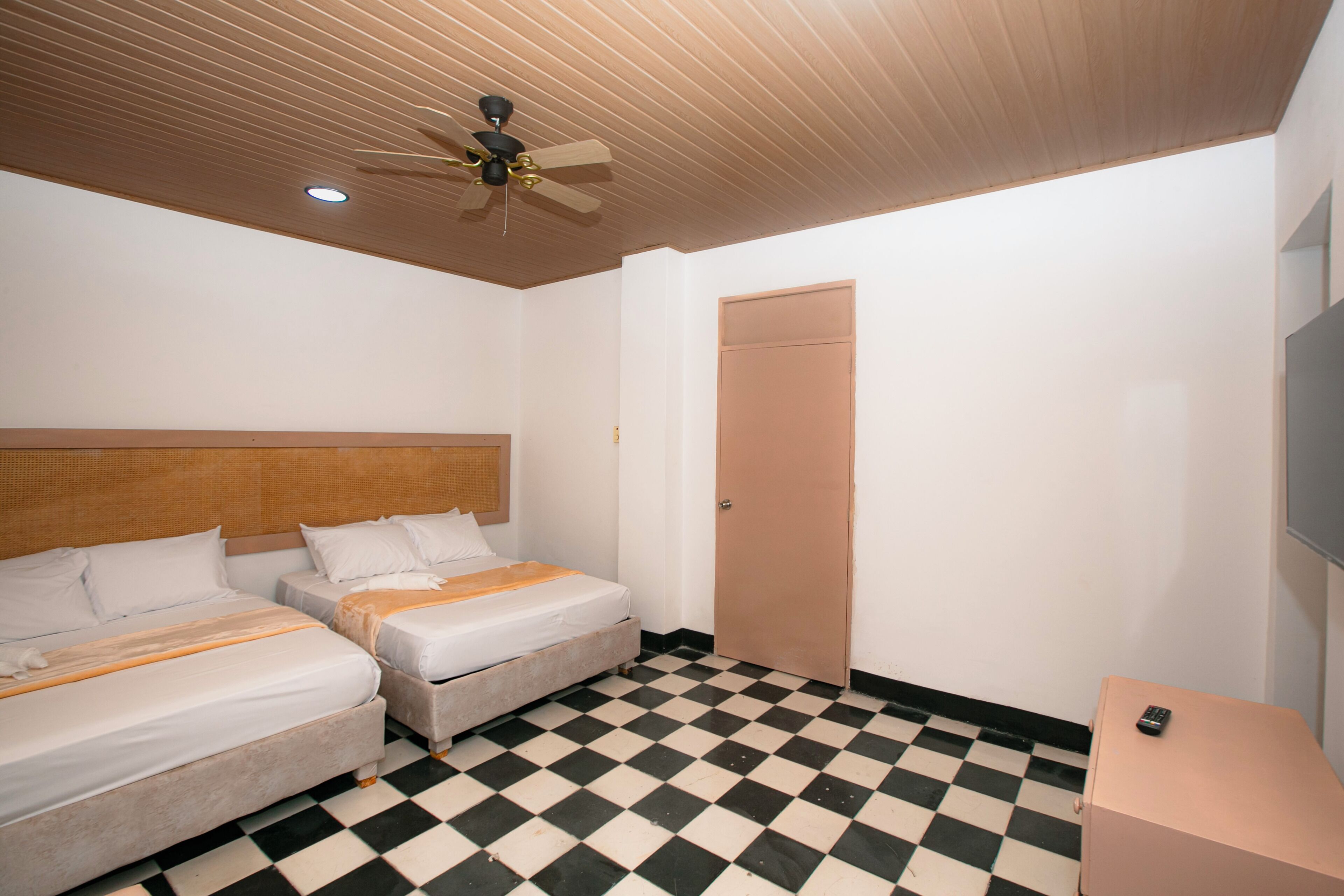 A hotel room with two beds, a ceiling fan, a checkered floor, and a door.