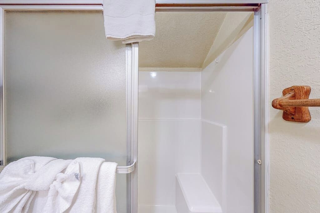 Une douche avec une porte en verre, un porte-serviettes en bois et une serviette blanche sur le sol.