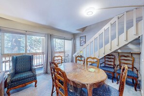 Ein Essbereich mit Holztisch und -stühlen, einer Treppe und großen Fenstern.