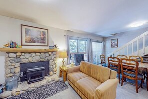 Ein Wohnzimmer mit Kamin aus Stein, einer Couch, einem Esstisch mit Stühlen und einer Treppe.