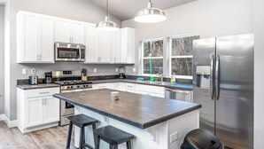 A modern kitchen with white cabinets, stainless steel appliances, and a central island with bar stools. - Secluded home with deck, grill, hot tub, fireplace, private beach, & W/D (Sagle)