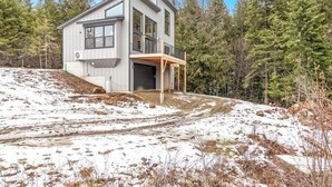 A modern two-story house with a large garage, surrounded by a forested area. - Secluded home with deck, grill, hot tub, fireplace, private beach, & W/D (Sagle)