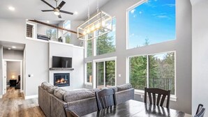 A modern kitchen with a fireplace, a dining area with a large table, and a loft space with a ceiling fan. - Secluded home with deck, grill, hot tub, fireplace, private beach, & W/D (Sagle)