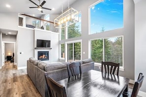 A modern kitchen with a fireplace, a dining area with a large table, and a loft space with a ceiling fan.