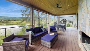Eine überdachte Terrasse im Freien mit Korbmöbeln, einem Grill und Blick auf einen See und Hügel.