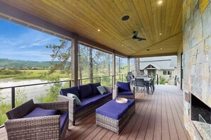 Eine überdachte Terrasse im Freien mit Korbmöbeln, einem Grill und Blick auf einen See und Hügel.