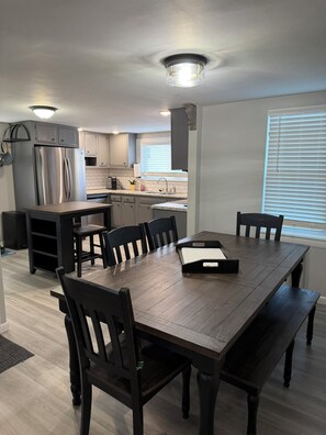 A modern kitchen with a built-in refrigerator, a dining table with chairs, and a window with blinds. - The Philipsburg Perch (North Philipsburg)
