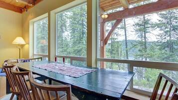 A dining table with chairs, large windows, and a wooden ceiling.