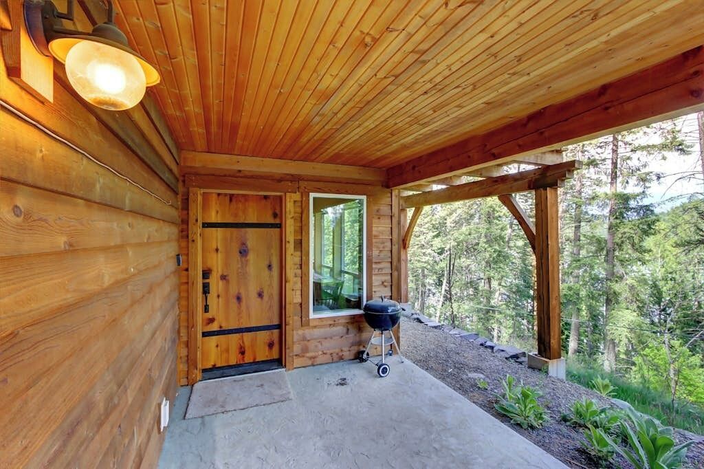 Une cabane en bois avec une véranda, une porte et un barbecue à l’extérieur.