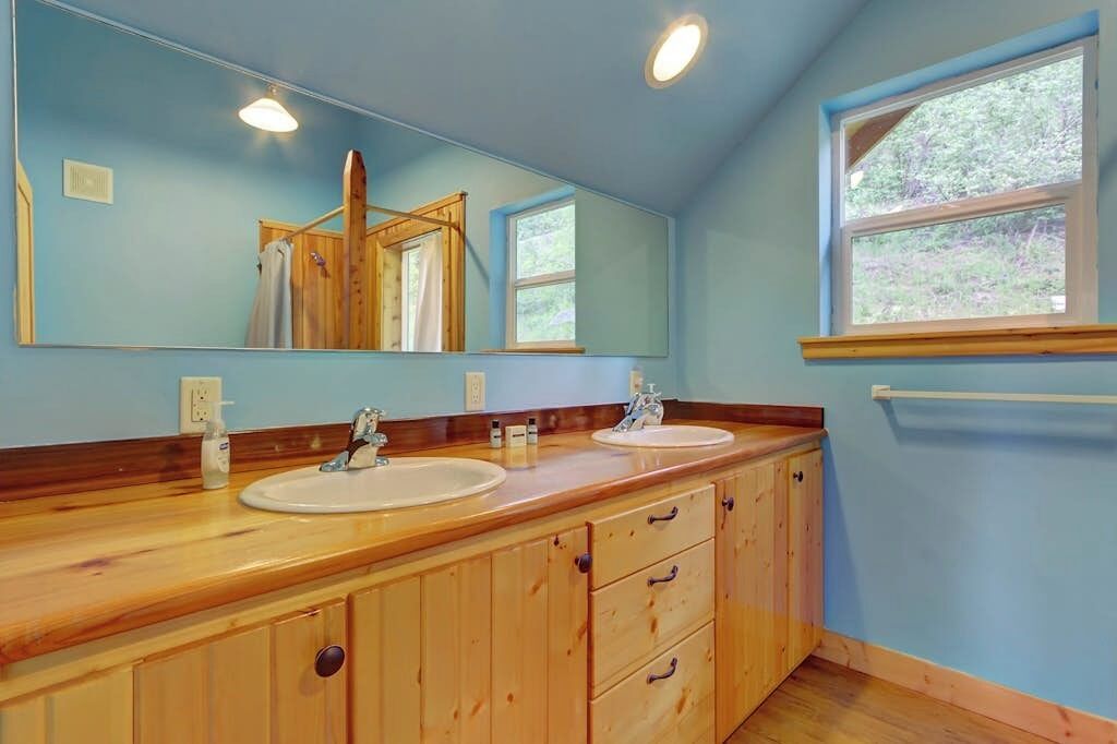 A bathroom with two sinks, wooden cabinets, a large mirror, and a window.