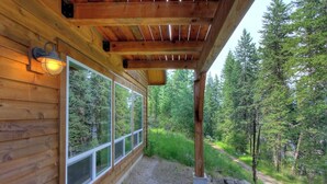 Een houten chalet met grote ramen, een overdekte veranda en een bebost landschap.