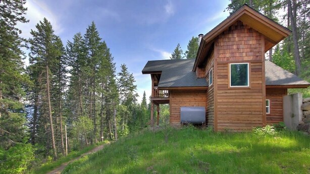 A wooden cabin with a balcony, surrounded by a forest.