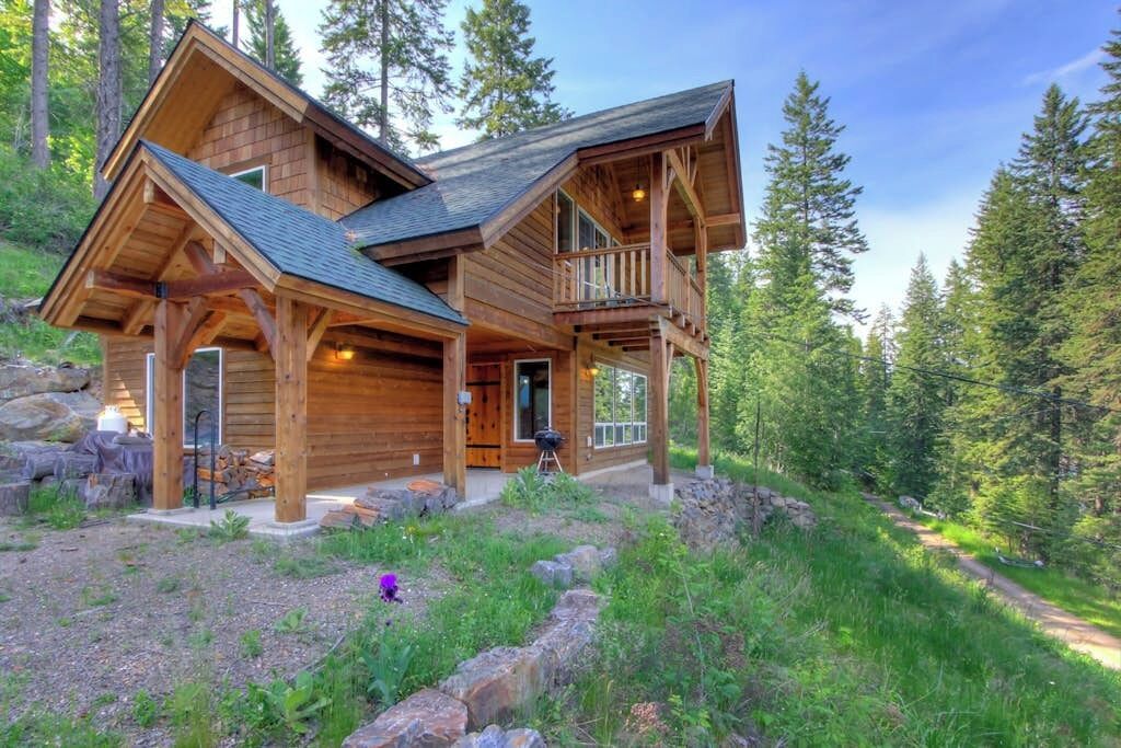 Une cabane en bois dotée d’un balcon, entourée d’un paysage boisé.