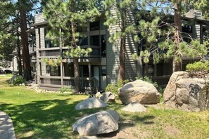 A multi-story building with a stone facade, large rocks in the foreground, and pine trees. - Three bedroom Condo w/Shared Pool, Hot Tub, Near Town and Ski Resort (Mammoth Lakes)