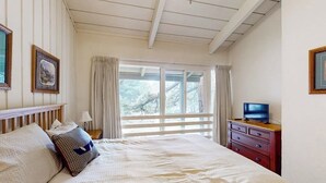 Ein Schlafzimmer mit einem Bett, einem Fernseher auf einer Kommode und einem Fenster mit Vorhängen.