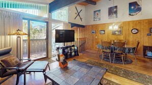 Ein geräumiges Wohnzimmer mit großem Fernseher, Holzmöbeln und einem Balkon mit Blick.