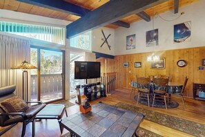 Ein geräumiges Wohnzimmer mit großem Fernseher, Holzmöbeln und einem Balkon mit Blick.