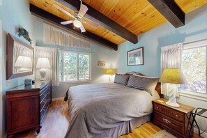Ein Schlafzimmer mit Bett, Nachttischlampen, einem Schminktisch, einem Deckenventilator und Fenstern.