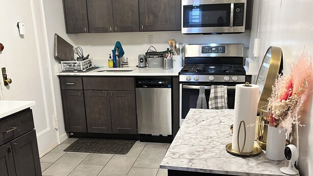 A modern kitchen with dark cabinets, stainless steel appliances, and a marble countertop.