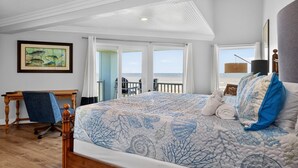 Une chambre avec un grand lit, un bureau et une chaise, une vue sur la plage et un tableau accroché au mur.