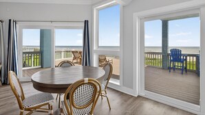 Une pièce avec une table ronde et des chaises, de grandes fenêtres et une vue sur la plage.