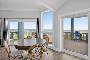 Ein Zimmer mit einem runden Tisch und Stühlen, großen Fenstern und Blick auf den Strand.
