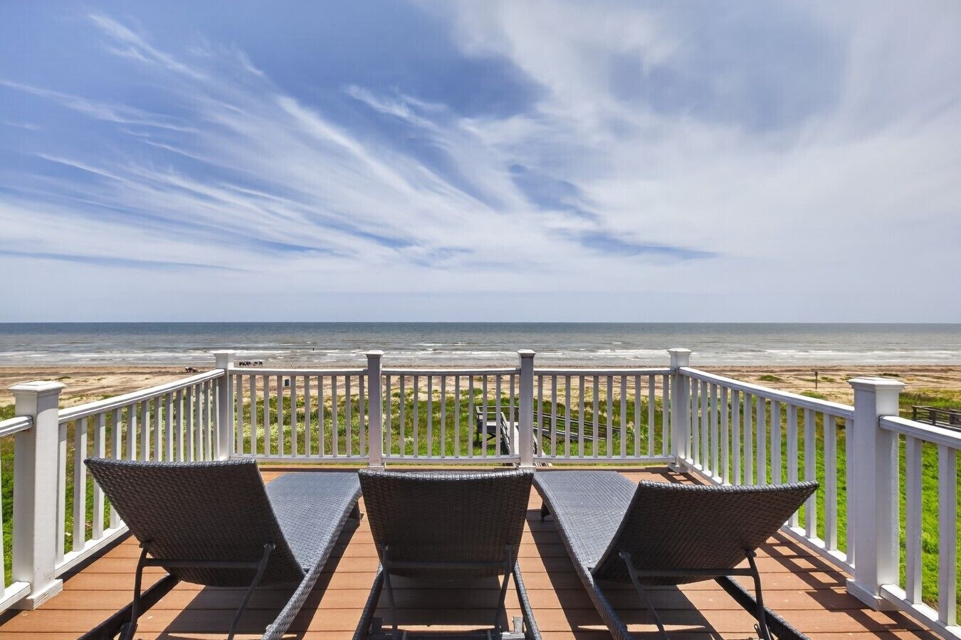 A balcony with wicker chairs and a view of the beach.