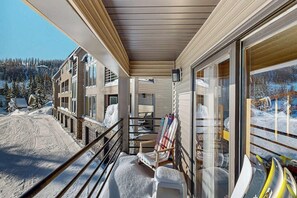 A covered balcony with a view of a snowy landscape, a chair, and a kayak.