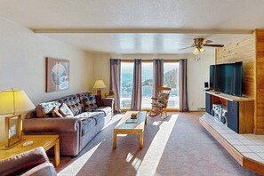 A living room with a sofa, coffee table, TV stand, and a view of a snowy landscape through large windows.