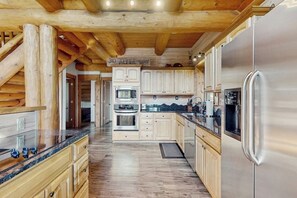Ein Holzblockhaus-Interieur mit einer Küche, die Holzschränke, Edelstahlgeräte und eine Holzbalkendecke zeigt.