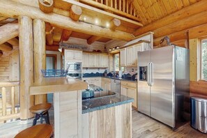 Ein rustikales Blockhaus-Interieur mit einer Küche, die Holzschränke, einen Edelstahlkühlschrank und eine Kücheninsel mit Granitplatte zeigt.