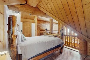 Ein Schlafzimmer in einer Blockhütte mit Bett, Holzbalken und Blick durch ein Fenster.