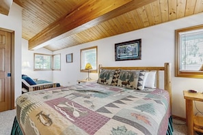 Une chambre avec un grand lit, des poutres apparentes en bois au plafond, une fenêtre avec des stores et un tableau encadré au mur.