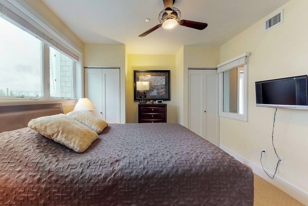 Une chambre à coucher avec un lit, un ventilateur de plafond, une télévision, une commode et une fenêtre.