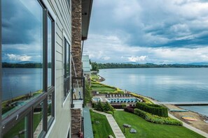 A lakeside view from a building with large windows, a swimming pool, and manicured landscaping.
