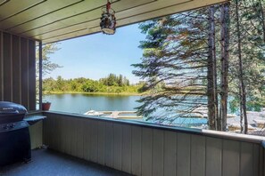 Uma área externa coberta com churrasqueira, vista para um lago e um píer.