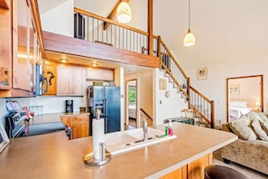 A modern kitchen with a central island, wooden staircase, and a cozy living area with a sofa.