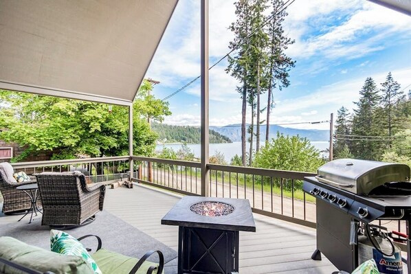 A covered deck with outdoor furniture, a fire pit, and a grill.