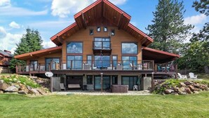 Een groot houten huis met een opvallend balkon, een overdekt terras en een verzorgd gazon.