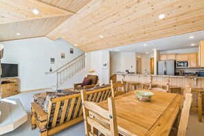A wooden dining area with a table and chairs, a kitchen with modern appliances, and a staircase leading to another level. - Updated Schweitzer Mt. condo w/ gas fireplace, full kitchen, & easy ski access (Sandpoint)