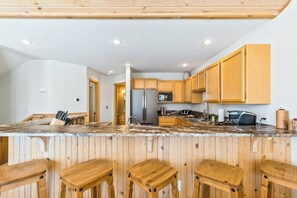 A kitchen with wooden cabinets, a stainless steel refrigerator, a granite countertop, and wooden stools. - Updated Schweitzer Mt. condo w/ gas fireplace, full kitchen, & easy ski access (Sandpoint)