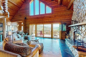 Ein rustikales Holzhaus-Interieur mit Kamin aus Naturstein, Holzmöbeln und großen Fenstern.