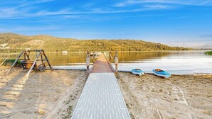 En träbrygga som leder ut till en sjö med båtar och en gunga vid stranden.