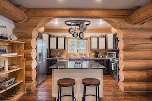 A log cabin kitchen with a central island, wooden cabinets, and a hanging pot rack.