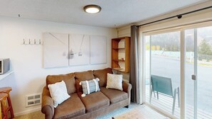 Ett vardagsrum med en brun soffa, en platt-TV, ett stort fönster och en skjutdörr i glas som leder ut till en balkong.
