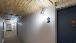 En hall med ett träpanelat tak, en skylt med siffran ’2’, en lampa och en dörr med en telefon.