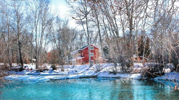 A red building by a clear blue river with snow on the ground.