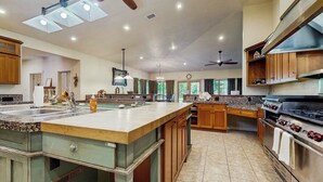A spacious kitchen with a large island, wooden cabinets, a built-in oven, and a ceiling fan.